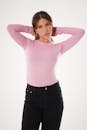 Stylish young woman in pink shirt posing casually against a white background.